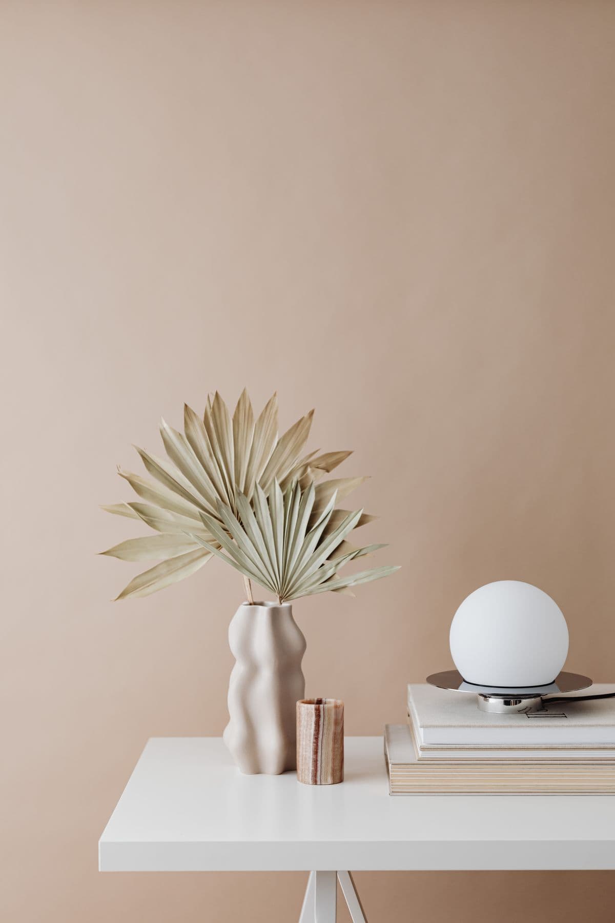 A warmly styled shelf with a ceramic vase, dried palm, and stacked books